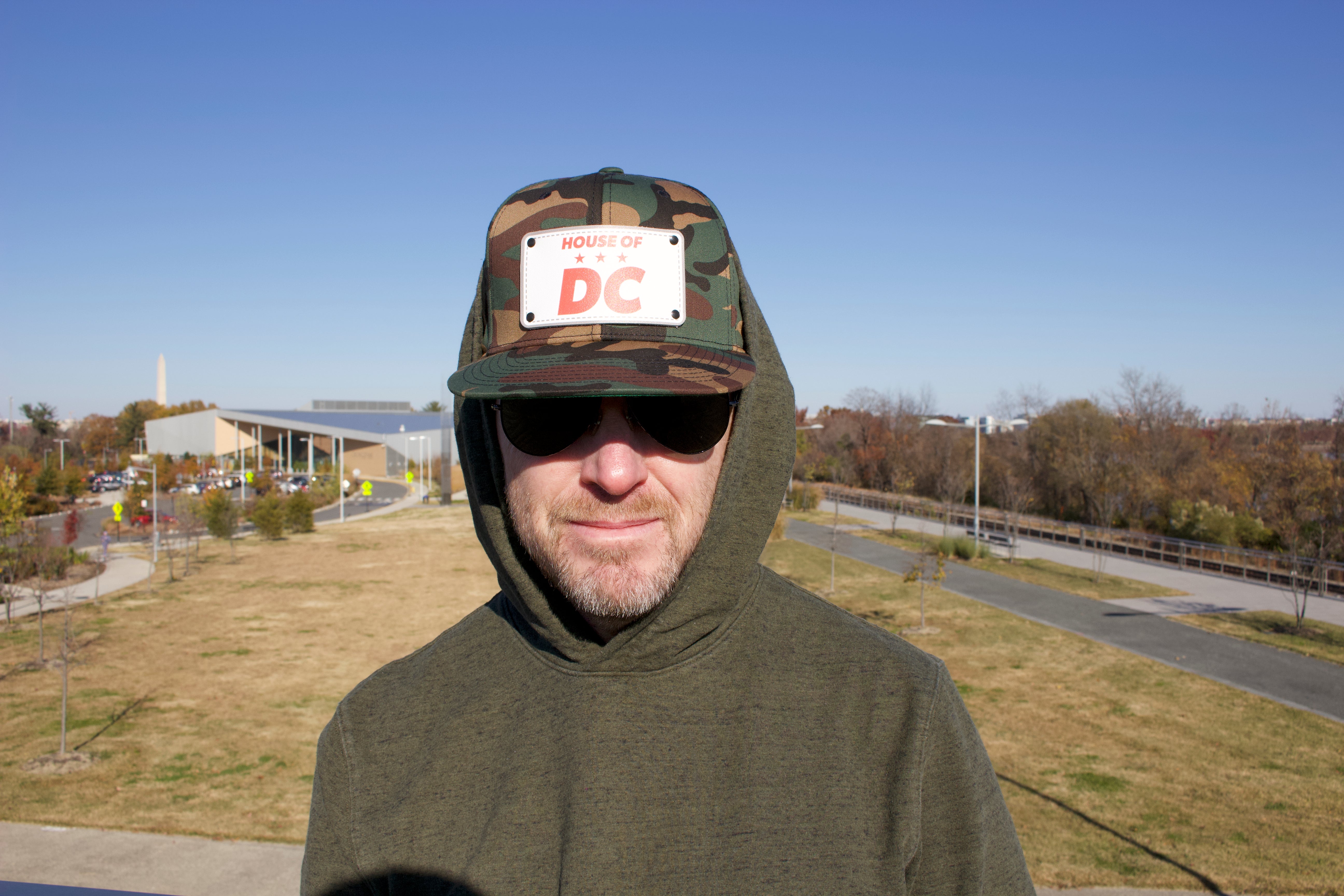 HOUSE OF DC KB, man wearing camo hat with green hoodie outdoors with Washington Monument in the background. 